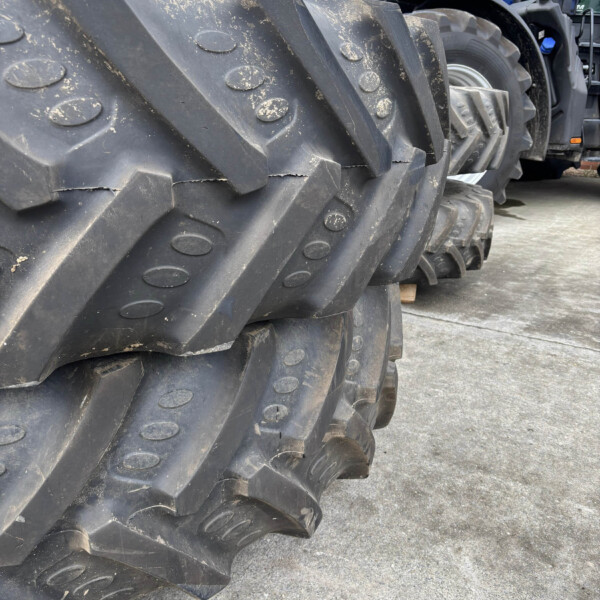 Close-up of muddy tractor tires stacked in a yard, with blue tractors visible in the background.