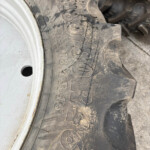 Close-up of a muddy tractor tire showing deep treads and a silver wheel rim visible on the left side of the image.