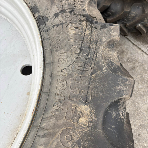 Close-up of a muddy tractor tire showing deep treads and a silver wheel rim visible on the left side of the image.