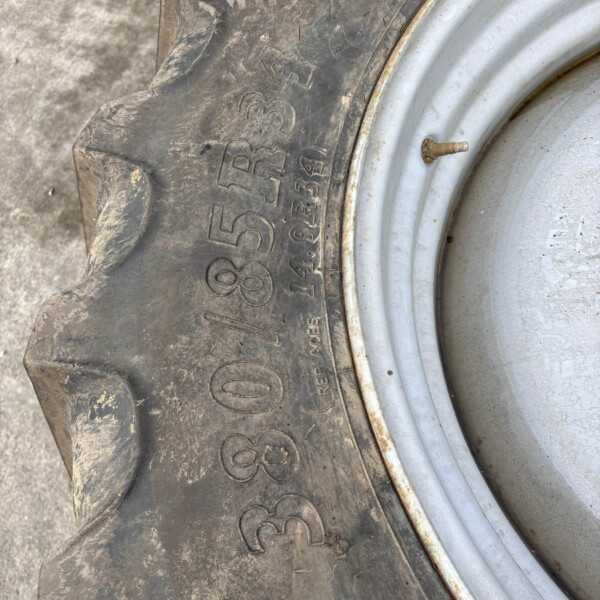 Close-up of a muddy tractor tire next to a light gray metal rim and a small valve stem protruding from the rim edge.
