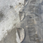 Close-up of a dusty tire with large embossed letters along the sidewall resting on rough pavement.