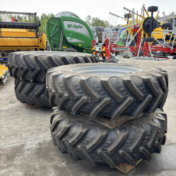 Stack of oversized tractor tires in the foreground with green McHale bale wrapper and other farming equipment in a yard behind them.