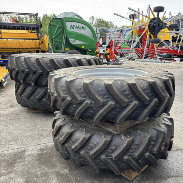 Stack of oversized tractor tires in the foreground with green McHale bale wrapper and other farming equipment in a yard behind them.