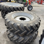 Two large off-road tractor tires stacked in a yard, with green farming machinery and other equipment in the background.