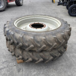 Large muddy tractor tire with metal rim lying on a wooden pallet in an outdoor equipment yard; other machinery and vehicles visible in the background.