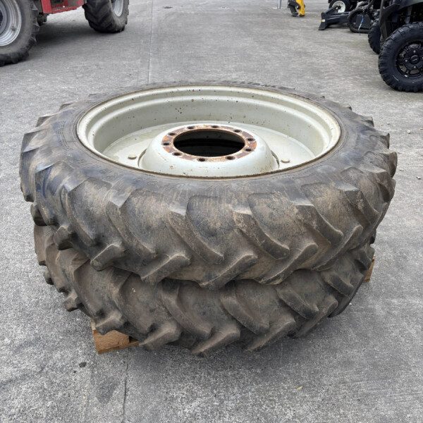 Large muddy tractor tire with metal rim lying on a wooden pallet in an outdoor equipment yard; other machinery and vehicles visible in the background.