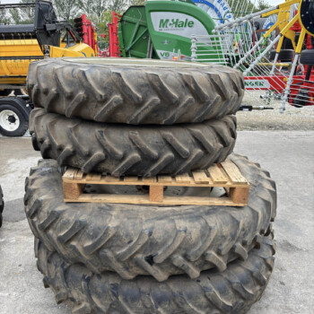 Stack of large muddy tractor tires stacked on a wooden pallet in a yard with farming machinery in the background.