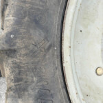 Close-up of a dusty black tire with embossed numbers beside a rusted metal rim edge.
