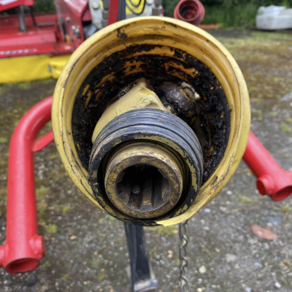 Close-up of a yellow circular hydraulic reel with black inner parts and red hoses in a muddy outdoor setting.