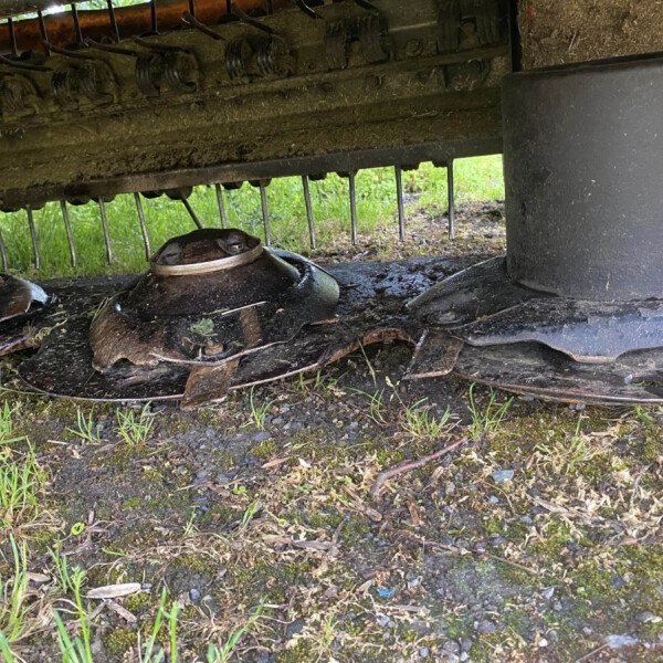 Underside of a dirty farming implement with row of metal tines and grime, seen from below.