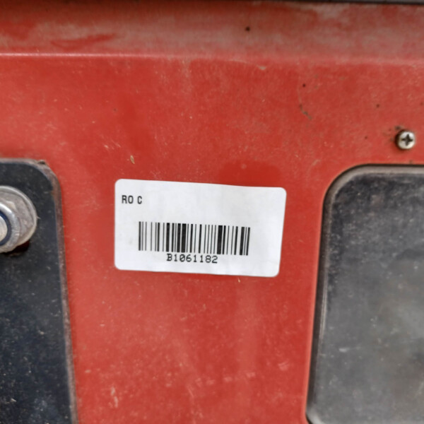 Close-up of a red metal panel with a white barcode label and a metal bolt on the left, surface dusty and worn.
