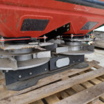 Close-up of a red industrial machine housing with exposed mounting bolts and circular cutting discs on a wooden pallet.