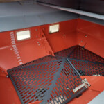 Interior of a red industrial cabinet with a perforated steel platform; a vertical measurement scale marked from 100 to 600 is visible on the left, and small rectangular windows are on the red wall.