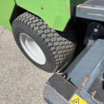 Close-up of a heavy tire on a green vehicle, with a rusted blue metal step nearby and asphalt ground visible.