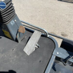 Close-up of a foot pedal and coiled black hose on a textured metal platform of heavy machinery.
