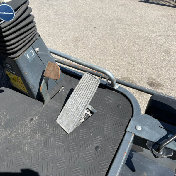 Close-up of a foot pedal and coiled black hose on a textured metal platform of heavy machinery.