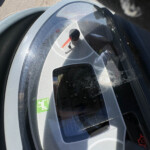 Close-up of a gray helmet visor with a red strap tab, viewed from above on a surface.
