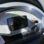 Close-up of a silver-gray helmet visor with a small green safety sticker and a red gauge visible through the glass.