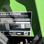 Close-up of a black identification plate on green agricultural equipment displaying the brand AMAZONE, model PH 1500 4WDi, serial numbers and a barcode/QR area.