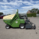Green Amazone Profihopper 1500 agricultural machine parked in a lot with red cars and a metal fence nearby.