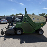 Green Amazone Profihopper machine in a parking lot beside a silver convertible car and a grey van, under a clear blue sky.