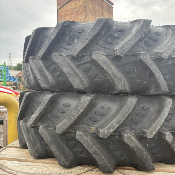Stack of large, rugged off-road tires stacked on a wooden pallet in an industrial yard or yard setting.