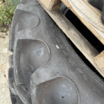 Close-up of a large black tire with wooden boards resting on top, outdoors in a yard setting.