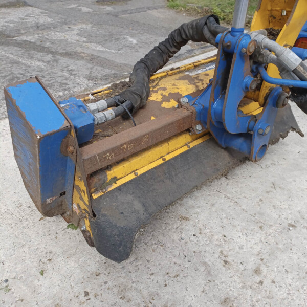 Close-up of a hydraulic, blue-and-yellow construction attachment with hoses and a gloved hand on a concrete surface.