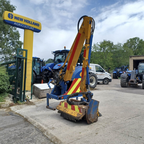 New Holland Agriculture sign on a yellow column with blue machinery in a dealership yard, trees in the background.