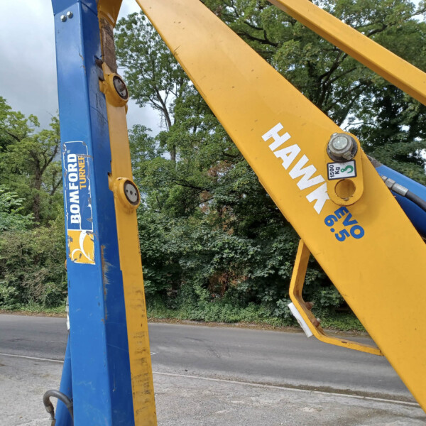 Close-up of blue and yellow construction crane arms connected by bolts, with trees in the background.
