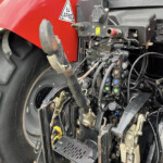 Close-up of a red tractor front with exposed hydraulic controls, hoses, and wiring near the wheel and chassis.