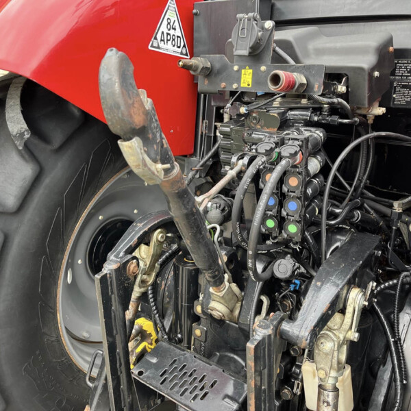 Close-up of a red tractor front with exposed hydraulic controls, hoses, and wiring near the wheel and chassis.