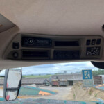 View of a truck cab interior with radio, climate controls, and dashboard, seen from the driver seat toward the windshield and yard outside.