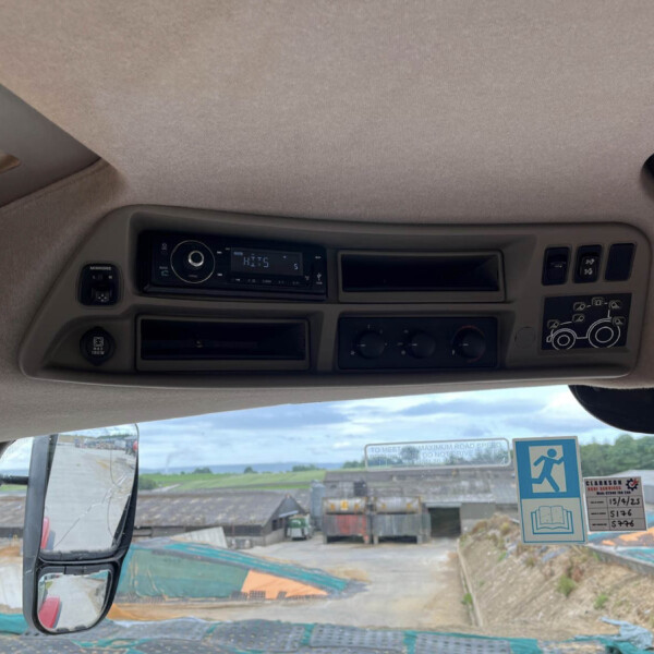 View of a truck cab interior with radio, climate controls, and dashboard, seen from the driver seat toward the windshield and yard outside.