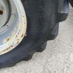 Close-up of a large tractor or heavy equipment tire with a rust-streaked white rim and weathered paint, resting on a concrete surface.