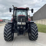 Front view of a red CASE IH tractor with oversized front tires in an outdoor yard beside a corrugated metal building.