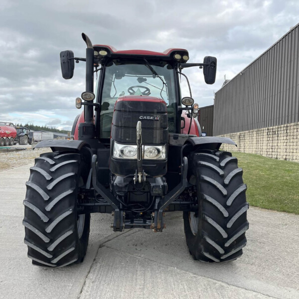 Front view of a red CASE IH tractor with oversized front tires in an outdoor yard beside a corrugated metal building.