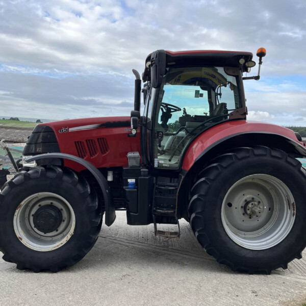 Red farm tractor with large tires, side view, parked on a concrete surface under a cloudy sky, cab visible.