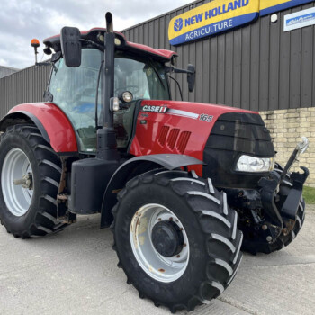 Front-left view of a red Case IH Puma 165 tractor parked beside a New Holland Agriculture building sign