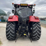 Rear view of a red tractor with oversized treads and visible hitch in an industrial yard.