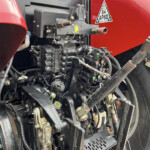 Close-up view of a red truck engine bay showing exposed wiring, hoses, and metal brackets with various connectors and a yellow warning label nearby.