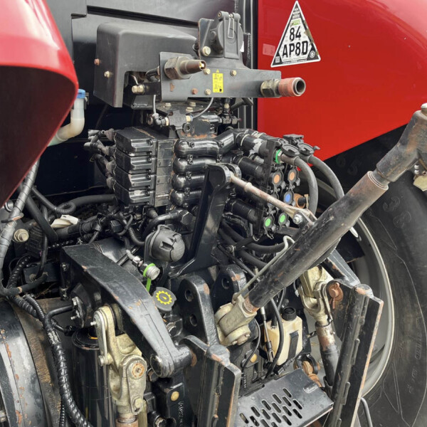 Close-up view of a red truck engine bay showing exposed wiring, hoses, and metal brackets with various connectors and a yellow warning label nearby.