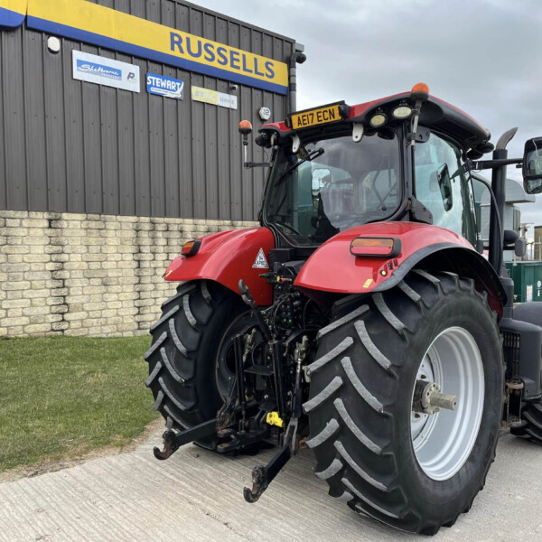 Red agricultural tractor with oversized rear tires parked beside a gray building with blue-and-yellow RussellS signs.