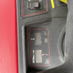 Close-up of a dusty vehicle control panel with a worn toggle switch and a yellow safety tag visible nearby.