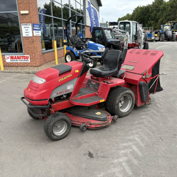 Red Countax ride-on mower in the foreground outside a building with other compact tractors displayed nearby at an equipment store.