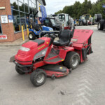 Red Countax ride-on mower in the foreground outside a machinery dealership, with blue utility vehicles and other equipment in the lot.",