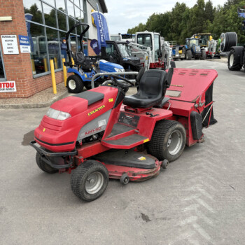 Red Countax ride-on mower in the foreground outside a machinery dealership, with blue utility vehicles and other equipment in the lot.",