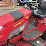 Red Countax lawn tractor with a black seat and hood, parked outside a brick building.