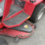 Close-up of red industrial vehicle steps and a large treaded tire, showing a black rubber step, warning sticker, and chipped paint.