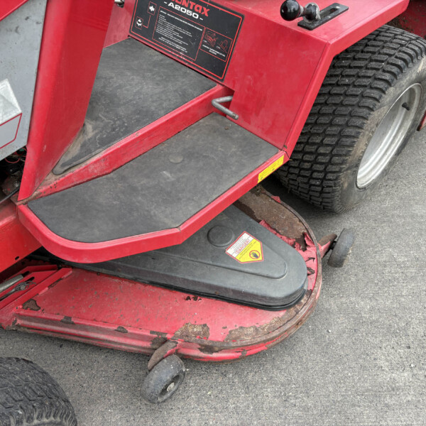 Close-up of red industrial vehicle steps and a large treaded tire, showing a black rubber step, warning sticker, and chipped paint.